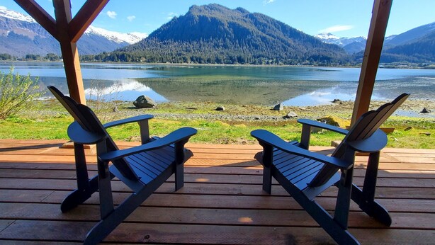 Une terrasse en bois avec deux fauteuils Adirondack donnant sur un lac et des montagnes.