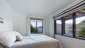 Une chambre à coucher avec un lit, une fenêtre donnant sur des montagnes et un lac, et une porte.