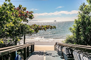 Uma escadaria de madeira que leva a uma praia, com vista para o oceano e um barco ao longe.