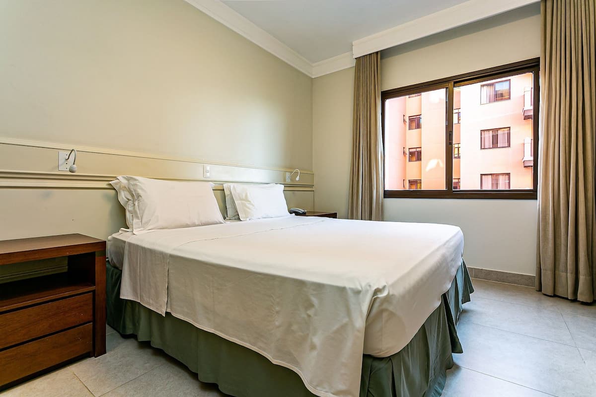 Une chambre d’hôtel avec un lit, une table de chevet et une fenêtre avec des rideaux.