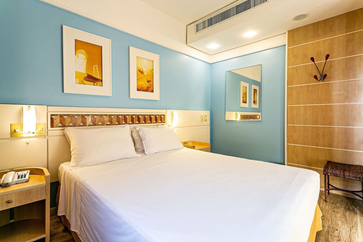 Une chambre d’hôtel équipée d’un lit, de tables de chevet, d’un téléphone, d’œuvres d’art accrochées aux murs et d’un miroir.
