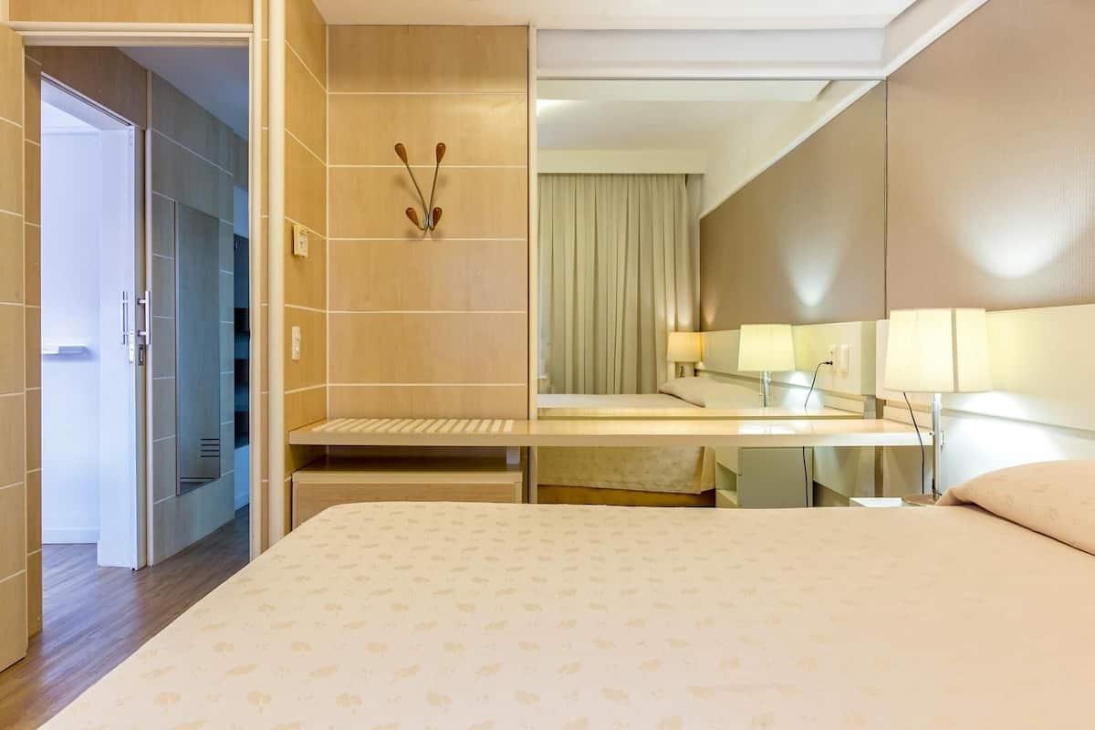 Une chambre d’hôtel comprenant un lit, une table de chevet, un miroir et une porte donnant accès à une salle de bain.
