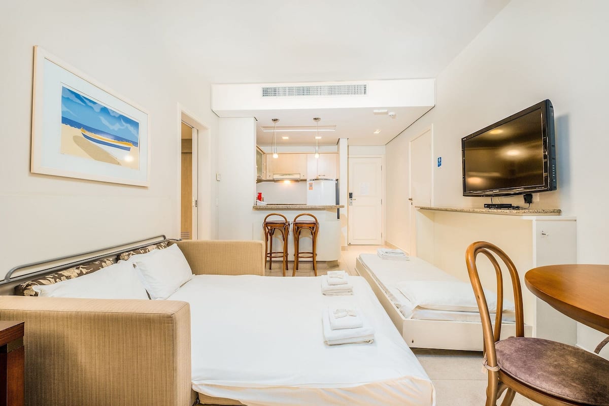 Une chambre d’hôtel comprenant un lit, un canapé, une télévision, un petit coin cuisine et un tableau au mur.