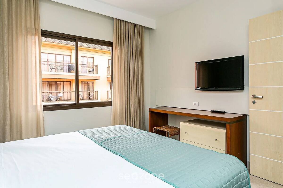 A hotel room with a bed, a desk with a television, a wardrobe, and a window with curtains.