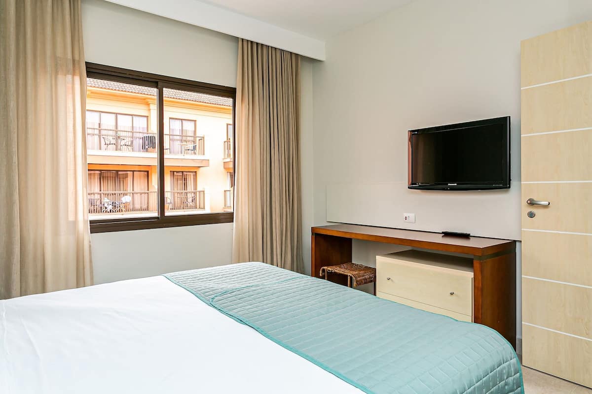 Une chambre d’hôtel équipée d’un lit, d’un bureau, d’une télévision et offrant une vue sur un bâtiment situé à l’extérieur.