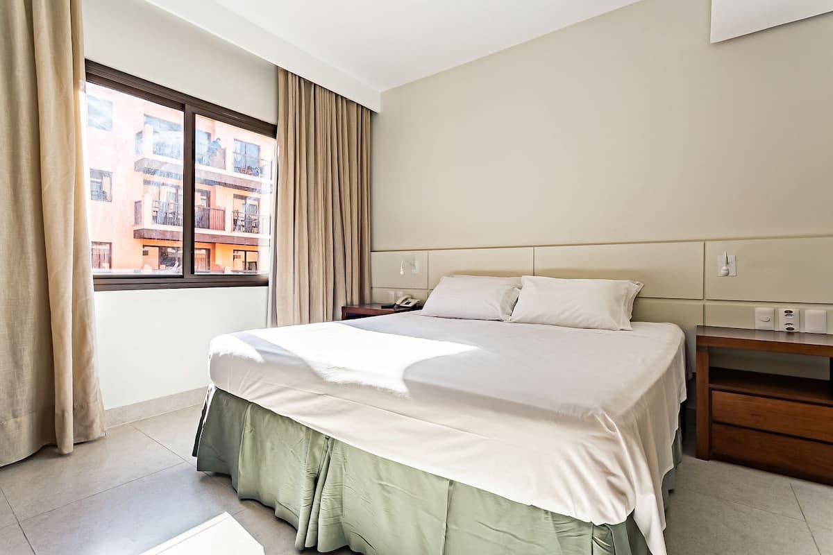 Une chambre d’hôtel avec un lit, une table de chevet, une fenêtre avec des rideaux et une vue sur les bâtiments environnants.
