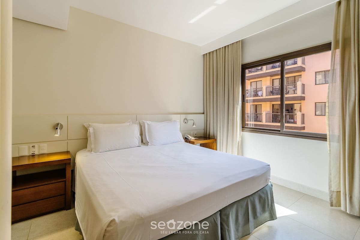 Une chambre d’hôtel avec un lit, des tables de chevet, une fenêtre avec des rideaux et une vue sur les bâtiments environnants.