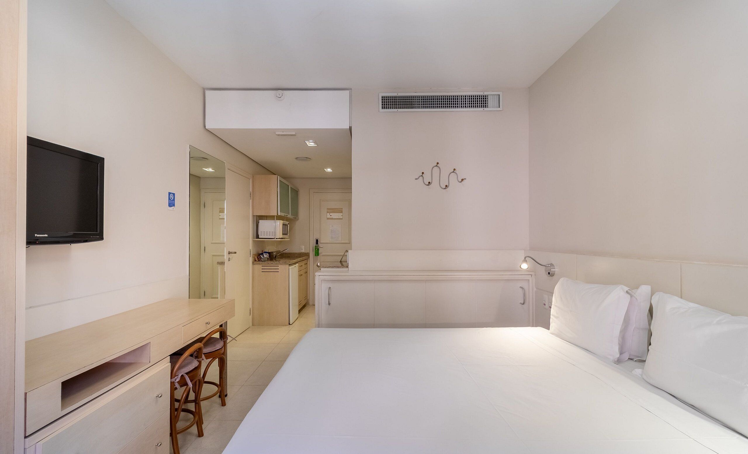 A hotel room with a bed, a desk with a chair, a television, a microwave, and a kitchenette.