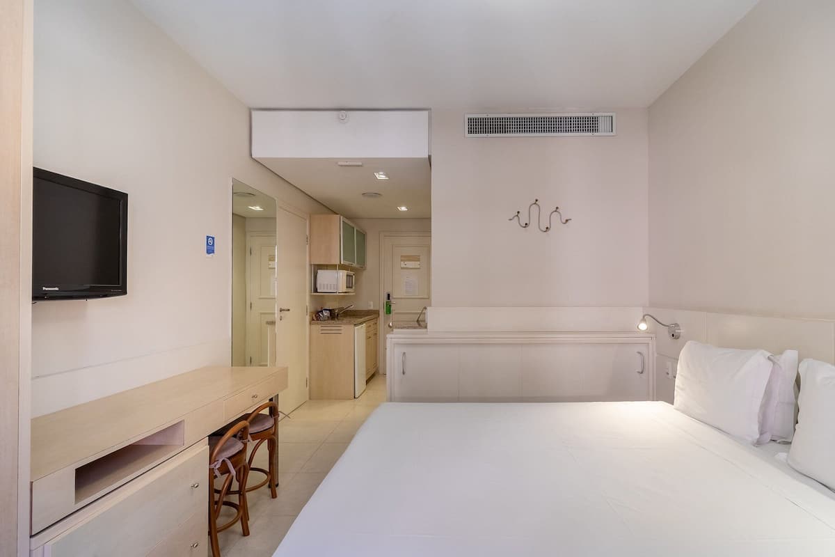 Une chambre d’hôtel comprenant un lit, un bureau avec une chaise, une télévision, un four à micro-ondes et une kitchenette.