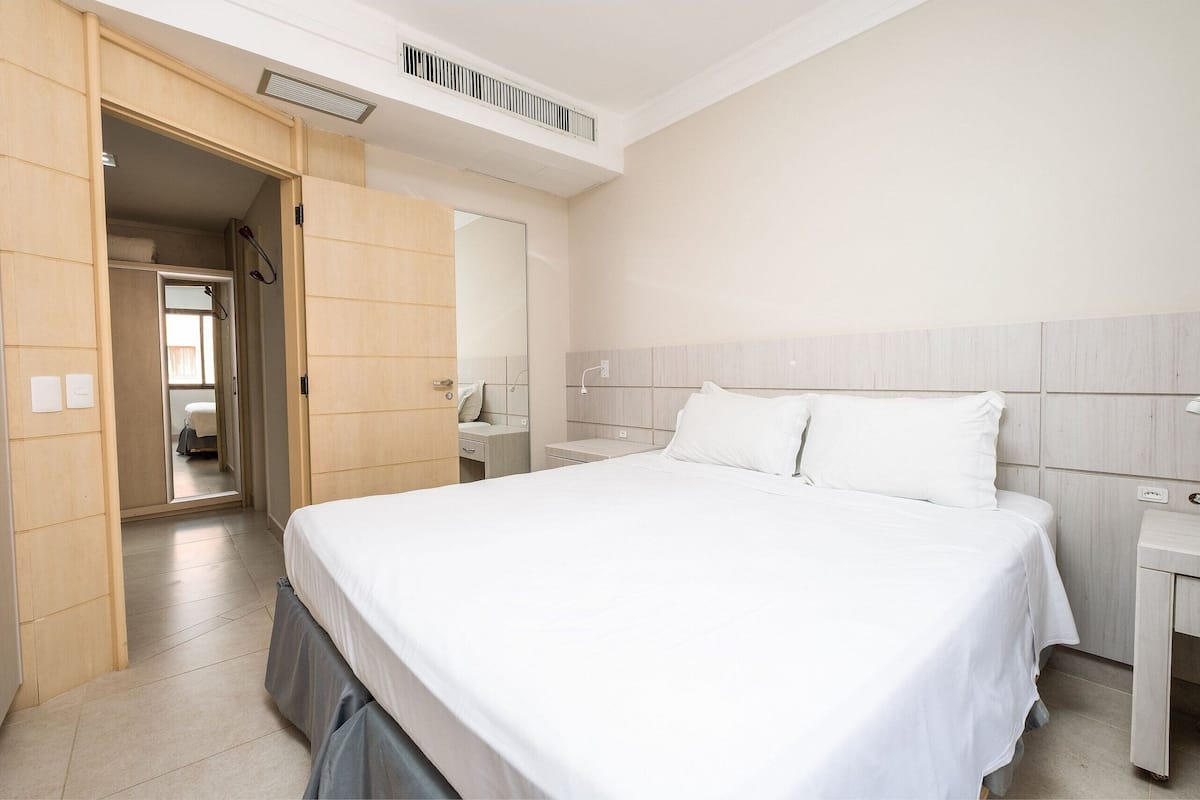 Une chambre d’hôtel comprenant un lit, une table de chevet, un miroir et une porte donnant accès à une salle de bain.