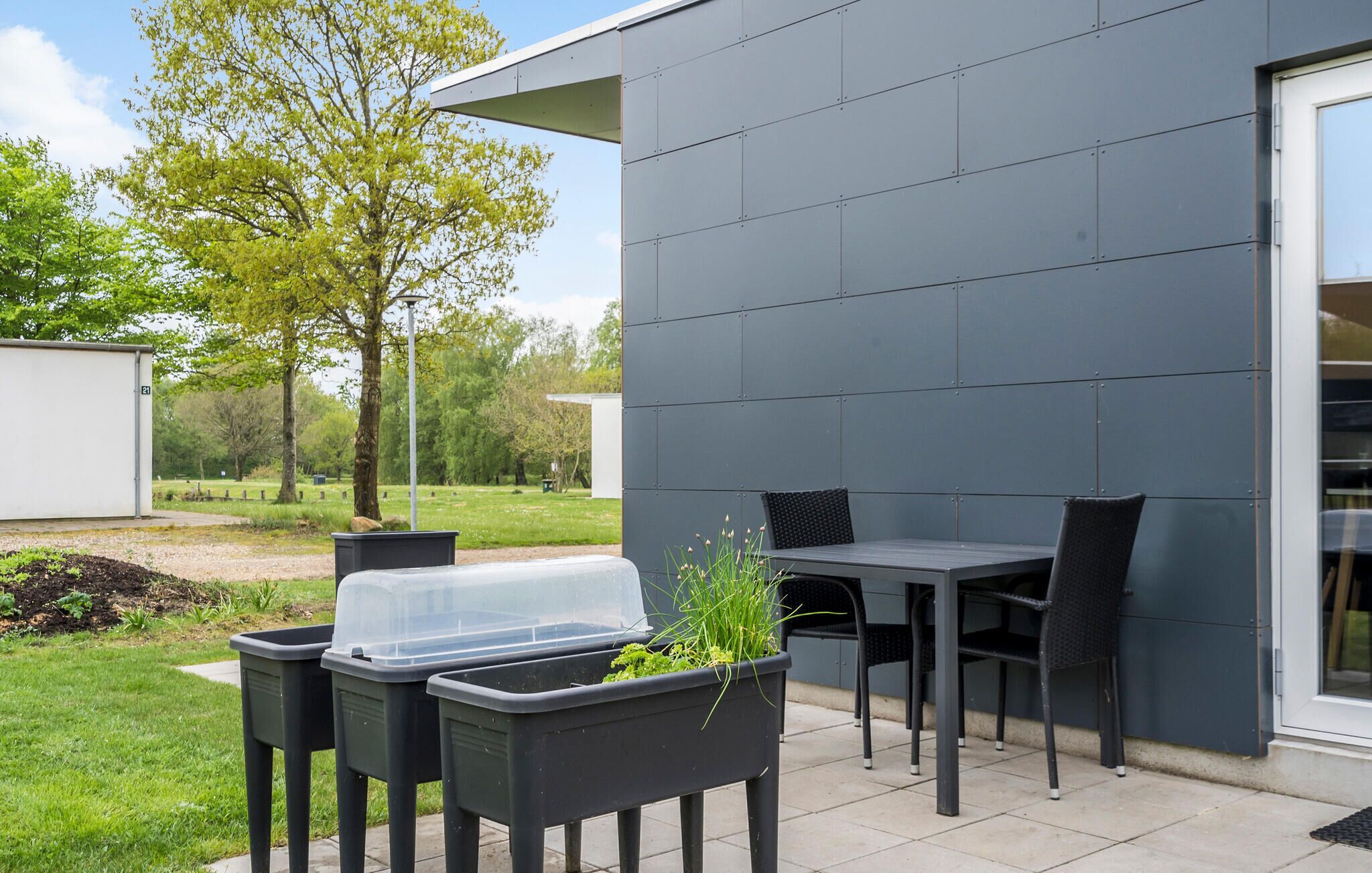 A patio area with a table and chairs, a trash bin, and a planter with greenery.