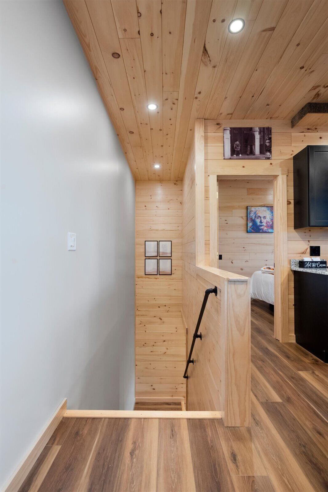 A modern interior with wooden walls and floors, a kitchen area with a black countertop, and a bed with a white headboard.