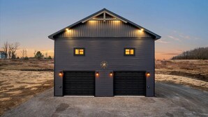A single-story building with a dark exterior, two garage doors, and a small window with a compass symbol. - Cozy Trailside Lodge #2 (Boonville)