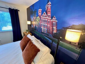 A hotel room with a bed, pillows, a nightstand, a lamp, and a wall mural of a building.