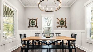 Une salle à manger avec une table en bois, des chaises noires et un lustre.