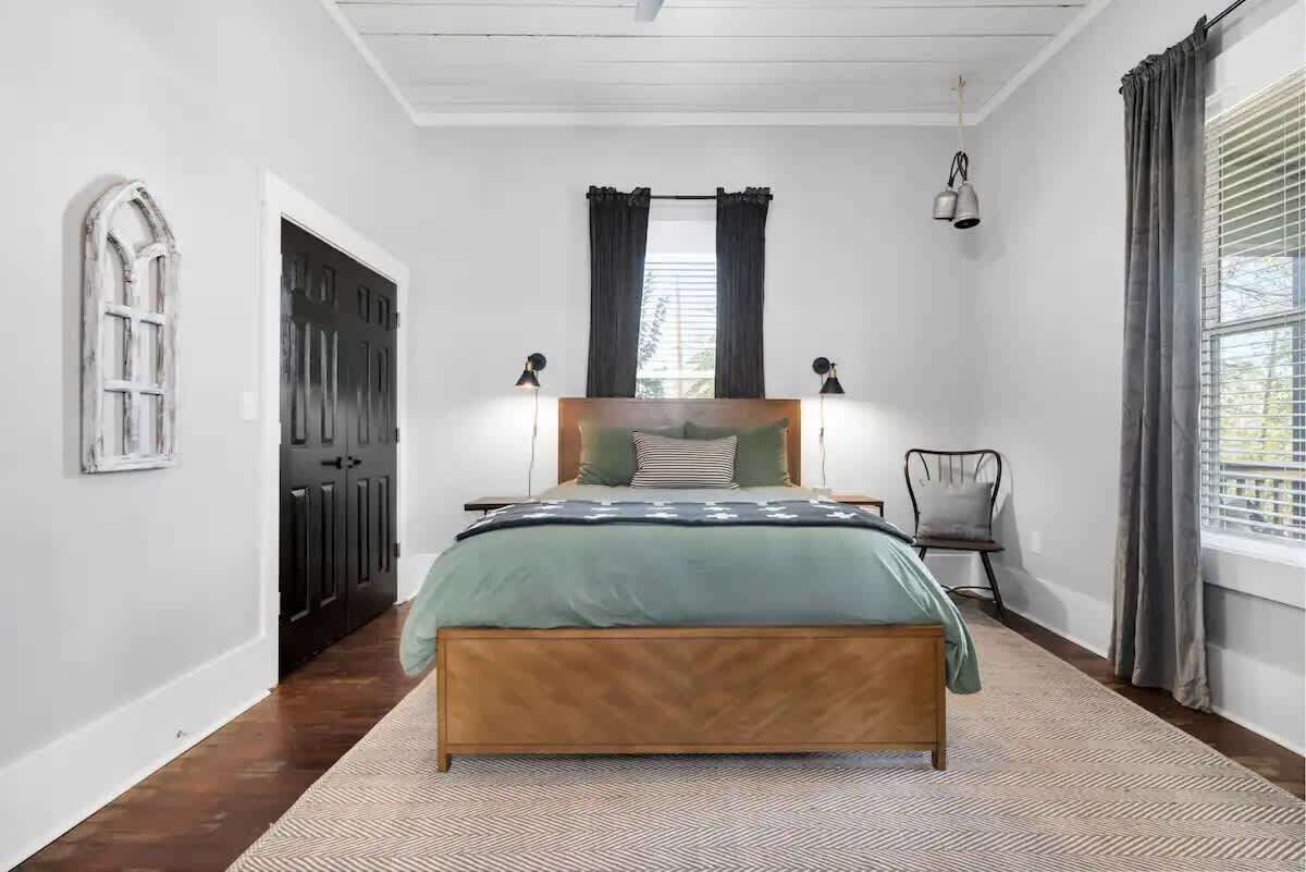 Un dormitorio con cama, una silla, una ventana con cortinas y una puerta.