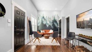 Un salon moderne avec une fresque représentant un paysage urbain, un canapé, deux fauteuils et une table basse.