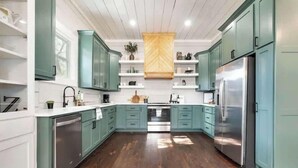 Une cuisine avec des armoires de couleur turquoise, un réfrigérateur en acier inoxydable et un dosseret en bois disposé en motif chevrons.