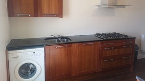 A compact kitchen with wooden cabinets, a Bosch washing machine, a gas stove, and a stainless steel sink. - 2 bedroom house near Athy, 45 minutes by train to Dublin (Athy)