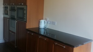 A kitchen with wooden cabinets, a black countertop, and stainless steel appliances including a refrigerator, oven, and microwave. - 2 bedroom house near Athy, 45 minutes by train to Dublin (Athy)