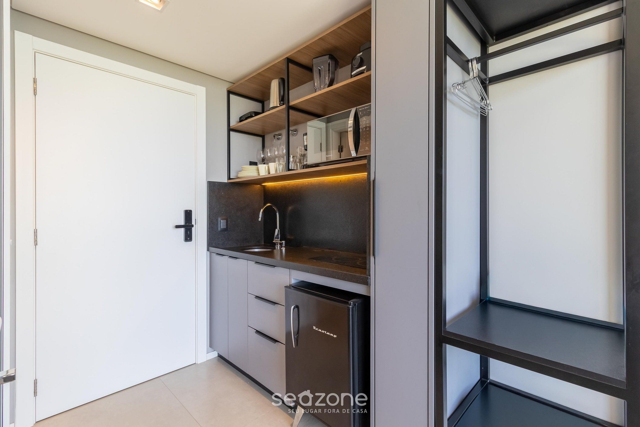 Una cocina compacta con electrodomésticos integrados, un lavamanos y un refrigerador pequeño.