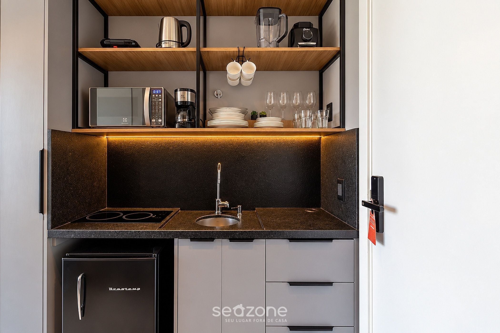 Eine kleine Küchenzeile mit eingebautem Herd, Spüle und kleinem Kühlschrank.