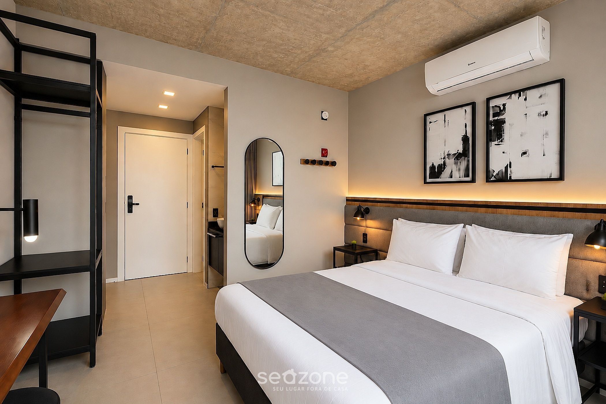 Una habitación de hotel con cama, mesitas de noche, espejo, armario y equipo de aire acondicionado.