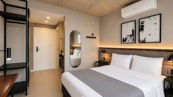 A hotel room with a bed, bedside tables, a mirror, a wardrobe, and an air conditioning unit.