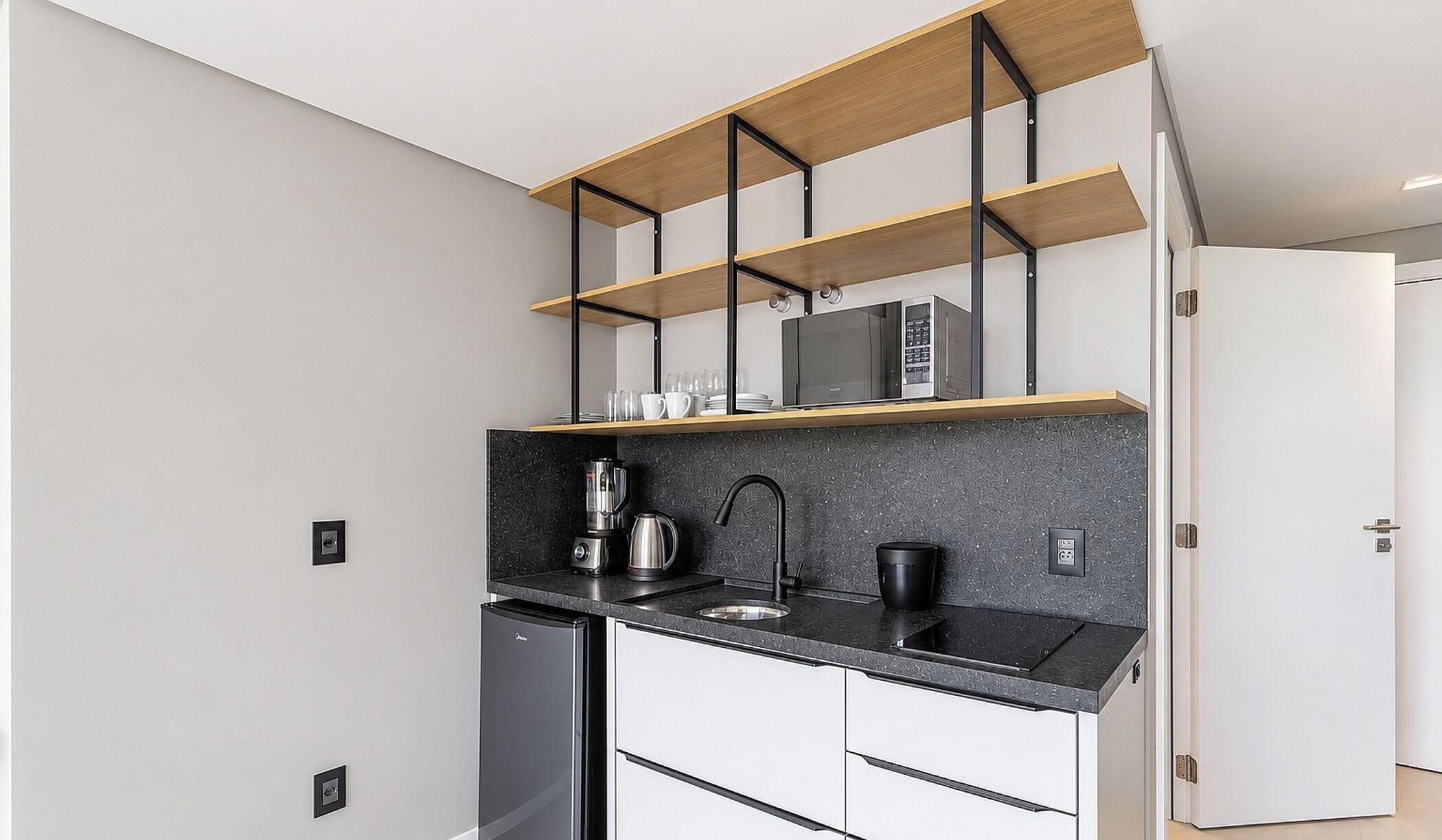 A compact kitchen with a black countertop, a coffee machine, a kettle, and a microwave on a shelf.