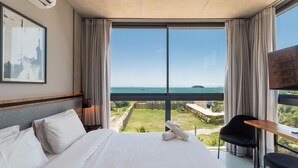 A hotel room with a large bed, a desk, and a view of the sea. - Spot Jurere sofisticação beira mar SPJs (Florianópolis)