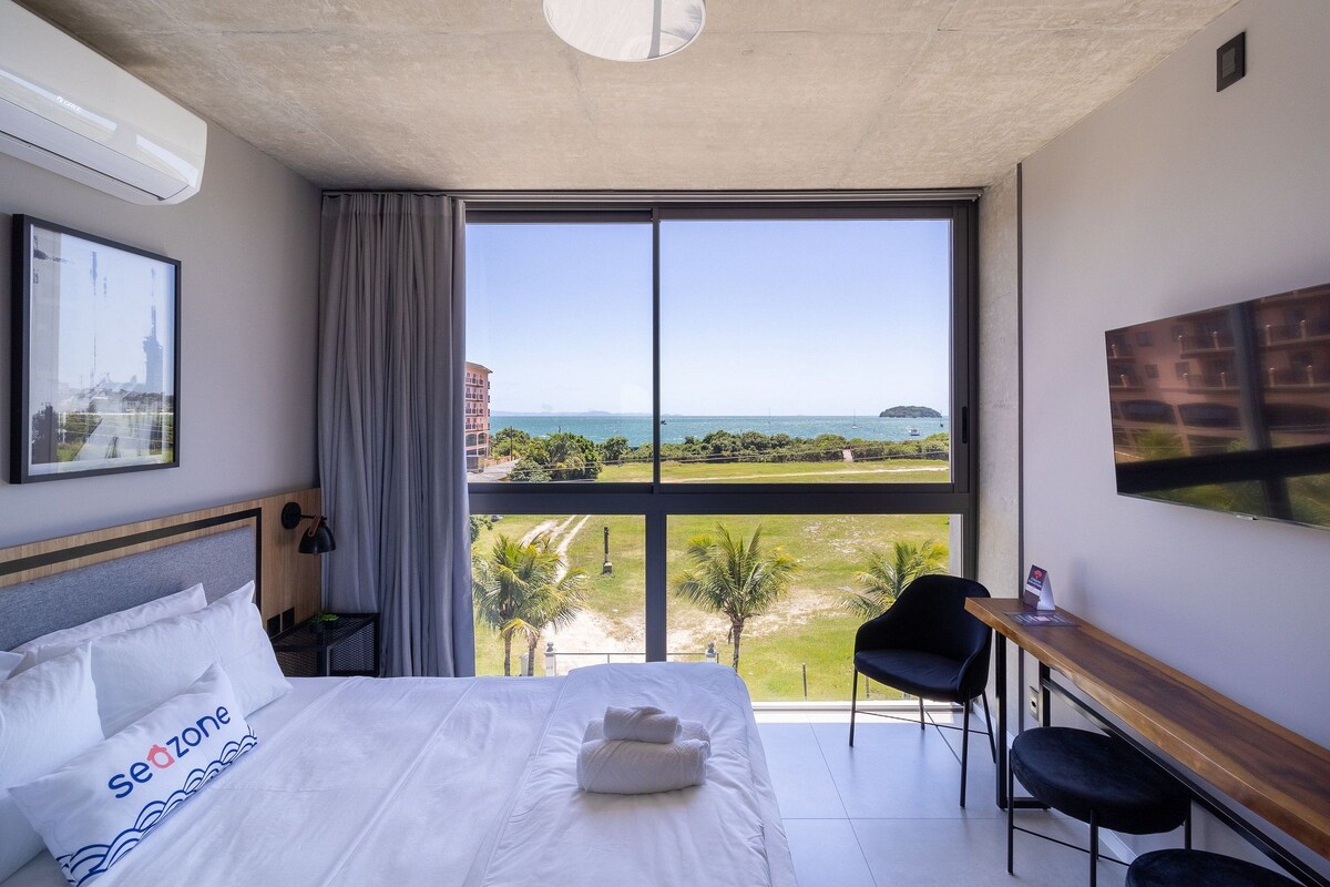 A hotel room with a large bed, a desk, a chair, and a view of the sea.