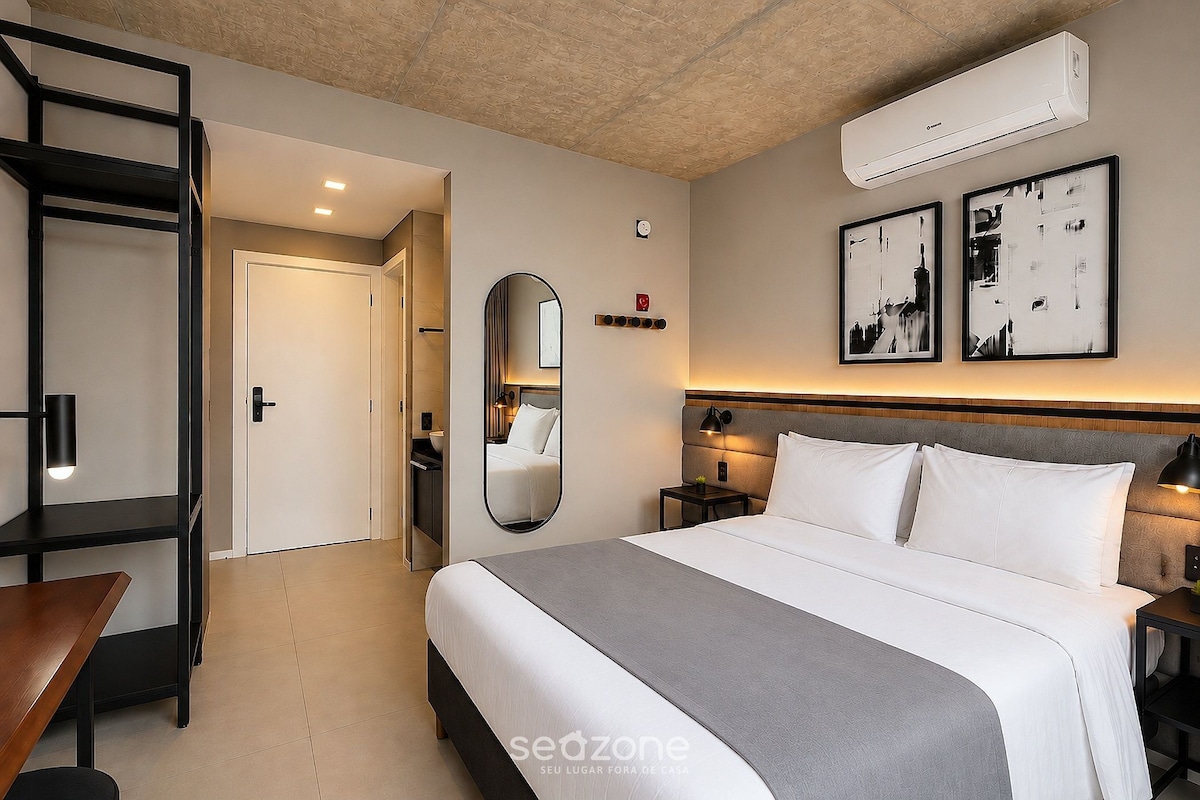 A hotel room with a bed, bedside tables, a mirror, a wardrobe, and an air conditioning unit.