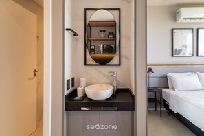 Un baño moderno con un lavabo redondo, un espejo y un estante empotrado con artículos de aseo.