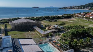 A resort with a pool, a wooden structure, and a view of the sea with boats. - Spot Jurere sofisticação beira mar SPJs (Florianópolis)