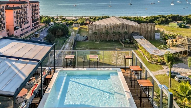 A rooftop pool with a view of the sea, surrounded by buildings and a wooden fence. - Spot Jurere sofisticação beira mar SPJs (Florianópolis)