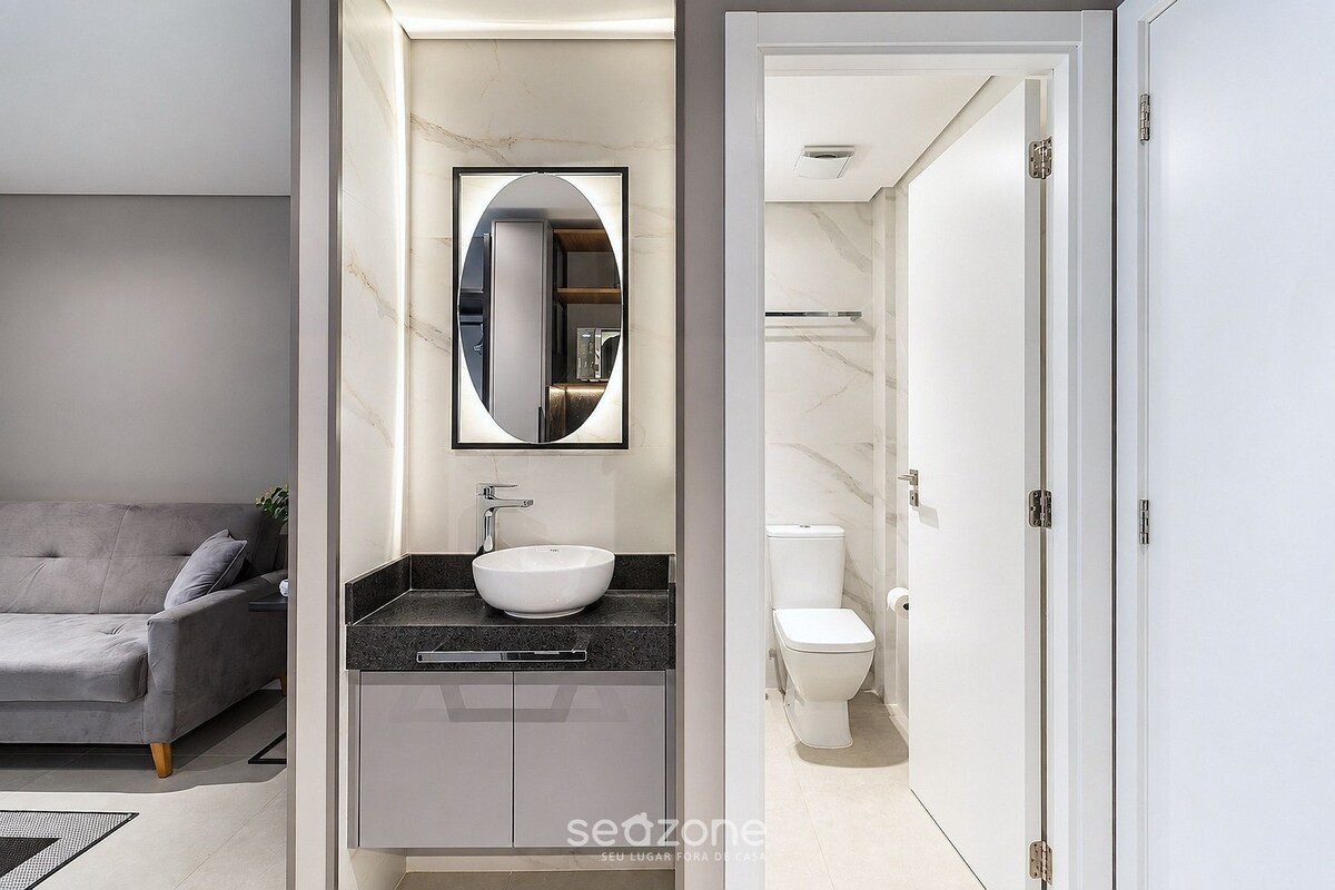 A modern bathroom with a large mirror, a white sink, and a toilet.