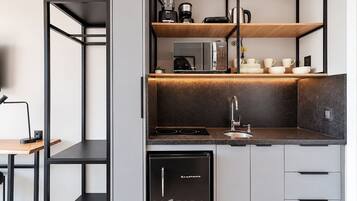 A compact kitchen with a dishwasher, a coffee maker, and a kettle on the countertop.