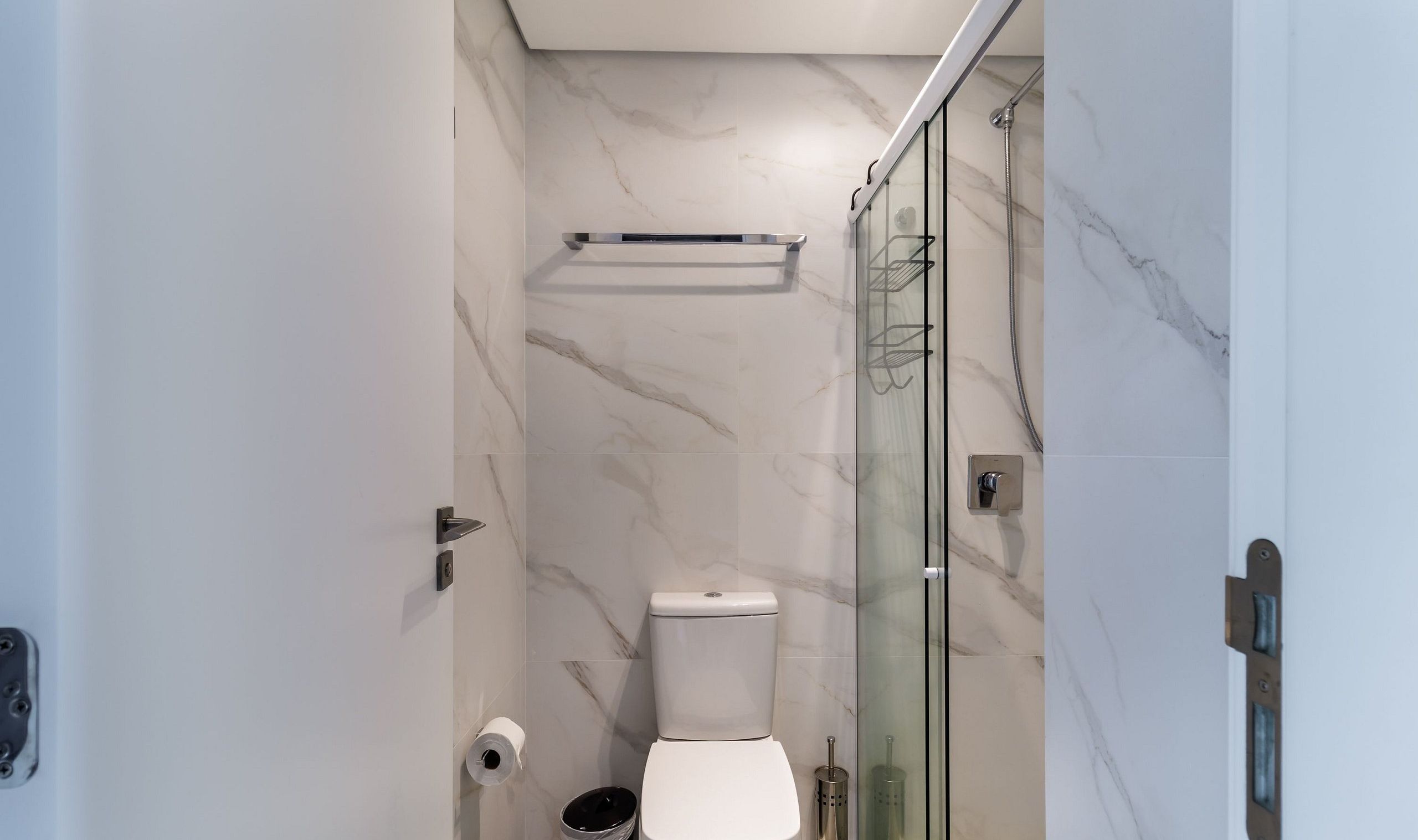 Een badkamer met toilet, een glazen douchecabine en een marmeren wand.