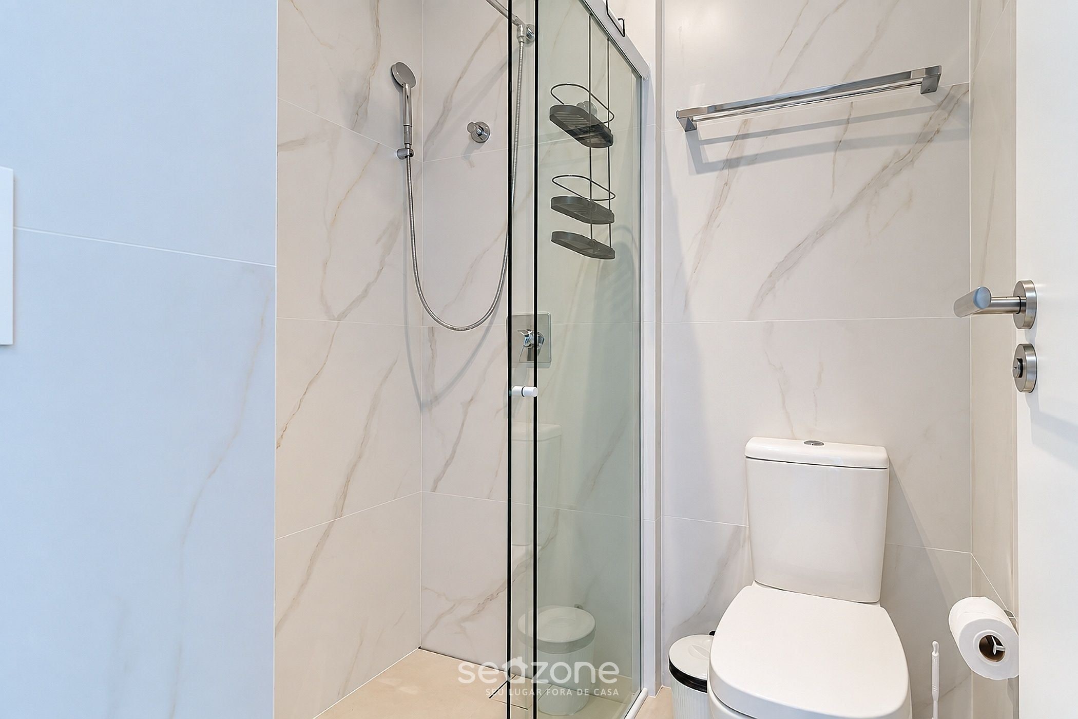 Un baño moderno con ducha envuelta en vidrio, inodoro y toallero.