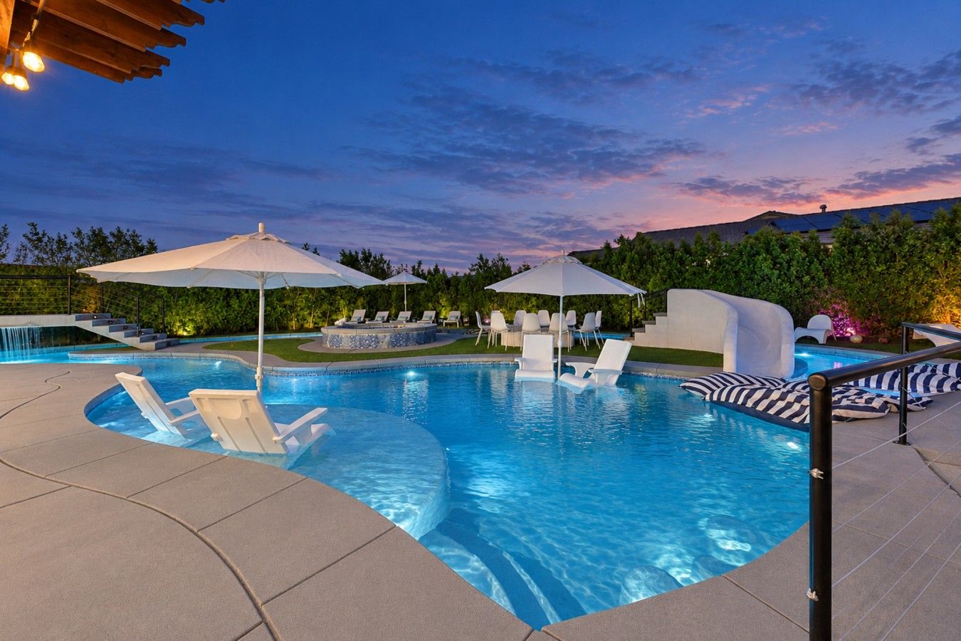 A swimming pool with lounge chairs and umbrellas, surrounded by a landscaped garden.