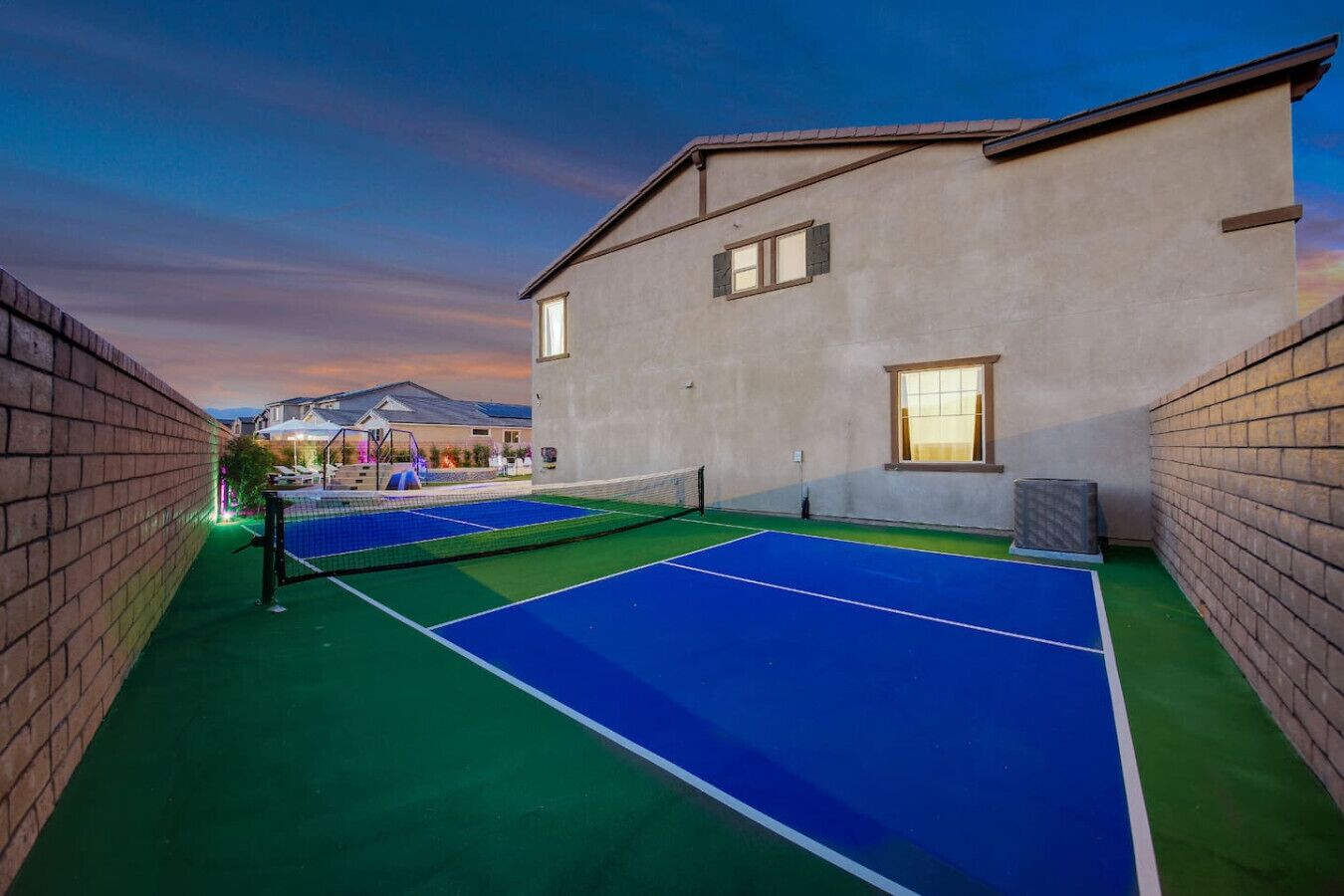 Una cancha de tenis junto a un edificio, con un muro de ladrillo en un lado y una ventana en el otro.