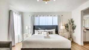 A modern hotel bedroom with a large bed, two bedside tables, a chandelier, and a potted plant. - Lazy River Pool+Spa+Pickleball+Game Room+BBQ+Golf (Coachella)