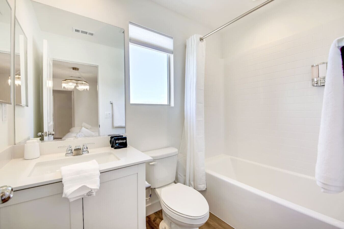 Et moderne badeværelse med en hvid vask, spejl og toilet. Der er badeforhæng og et håndklæde hængende på væggen.