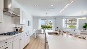A modern kitchen with a central island, white cabinetry, and a view of the outdoors. - Lazy River Pool+Spa+Pickleball+Game Room+BBQ+Golf (Coachella)