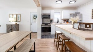 A modern kitchen with white cabinets, stainless steel appliances, and a wooden dining area. - The Harbor @ Lighthouse Lodge – Lakefront Home with Covered Porch & Boat Slip Access (Kimberling City)