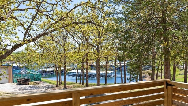 A wooden bench overlooking a lake with trees and a dock. - The Harbor @ Lighthouse Lodge – Lakefront Home with Covered Porch & Boat Slip Access (Kimberling City)