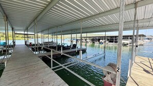 A covered dock area with boats, a wooden walkway, and a view of the water. - The Harbor @ Lighthouse Lodge – Lakefront Home with Covered Porch & Boat Slip Access (Kimberling City)