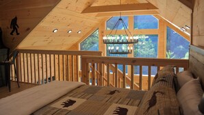 Ein Schlafzimmer mit schrägverdeckter Decke, einem Kronleuchter, Blick durch große Fenster und einem Hollerleger.