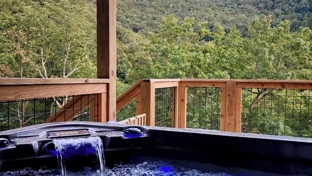 Ein Whirlpool mit Holzterrasse und Blick auf einen bewaldeten Hang.