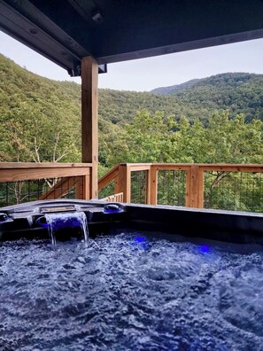 Un bain à remous avec une terrasse en bois et une vue sur une colline boisée.